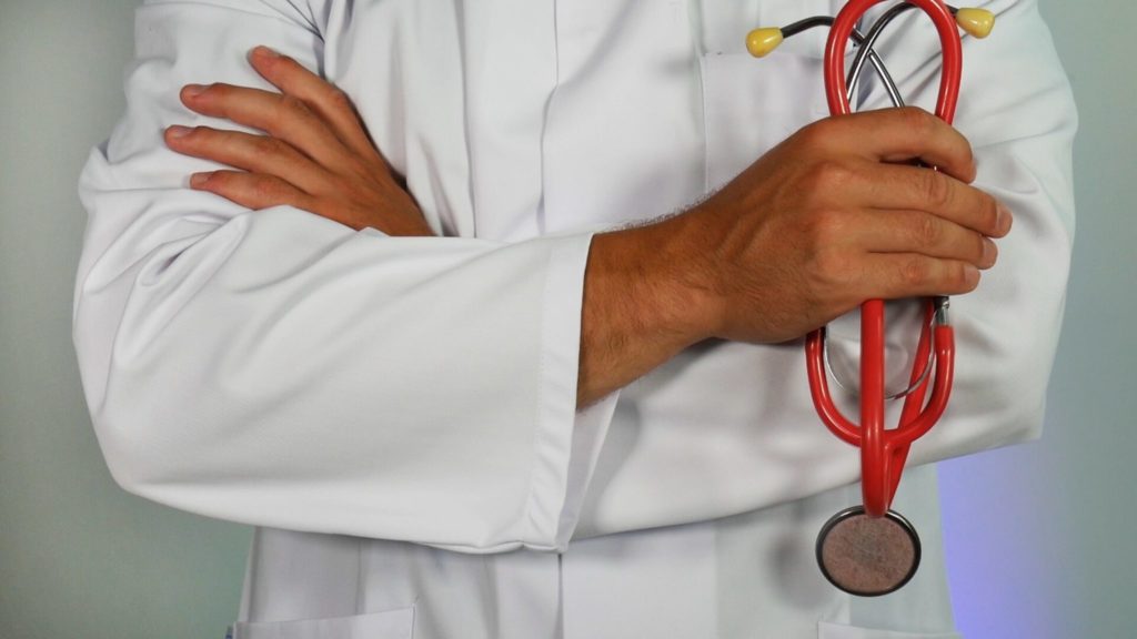 doctor in white coat holds red stethoscope